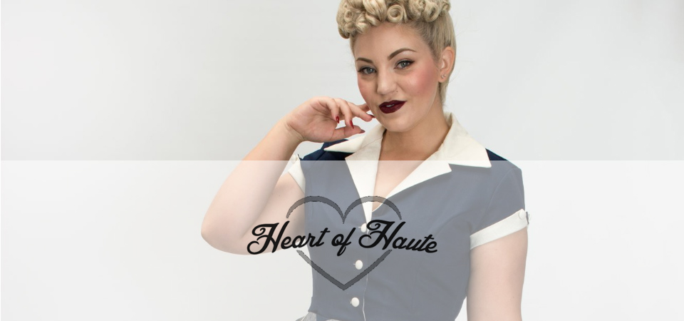 Heart of Haute Frau mit Poodle-Frisur in einem blauen 50er Jahre Kleid mit weißem Kragen, Logo der Marke Heart of Haute