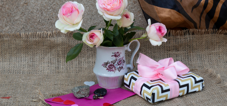 Gutscheine Ein hübsch verpacktes Geschenk liegt neben einer Vase mit rosa Blumen