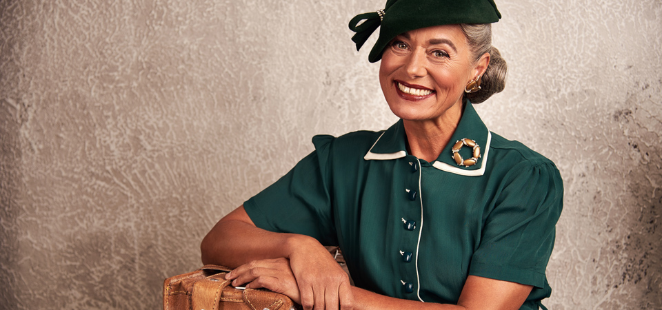 Mode der 40er Jahre Eine ältere Frau trägt ein grünes 40er Jahre Kleid mit Hut und lacht in die Kamera
