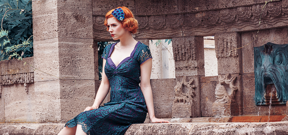 Mode der 30er Jahre Eine Frau in einem grünen Spitzenkleid im Stil der 1930er Jahre sitzt an einem Brunnen