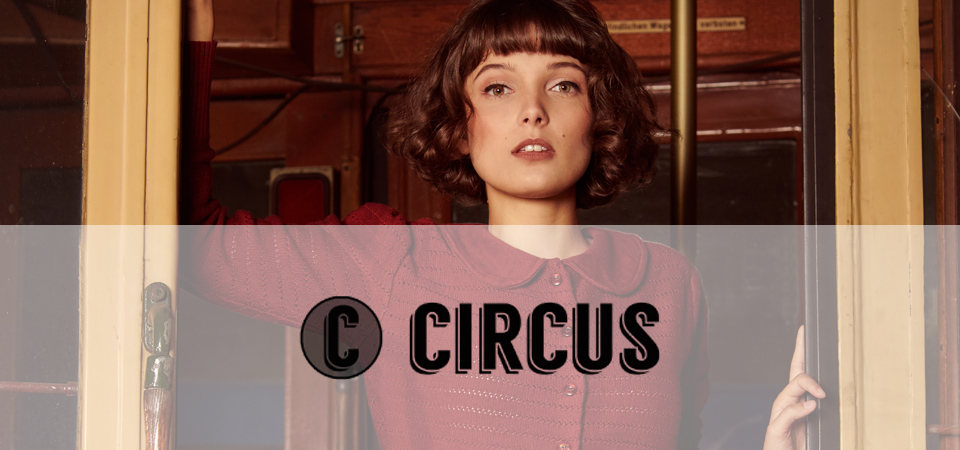 Circus Eine dunkelhaarige junge Frau trägt eine weinrote Strickjacke im 50er Jahre Stil, Logo der Marke Circus