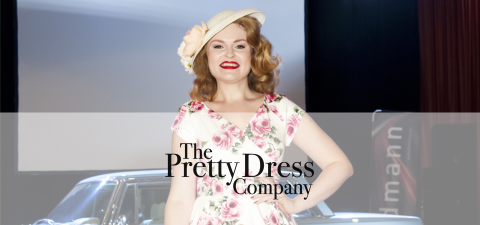 Pretty Dress Company Eine Frau trägt ein geblümtes Kleid und einen Hut im 50er Jahre Stil, Logo der Marke Pretty Dress Company